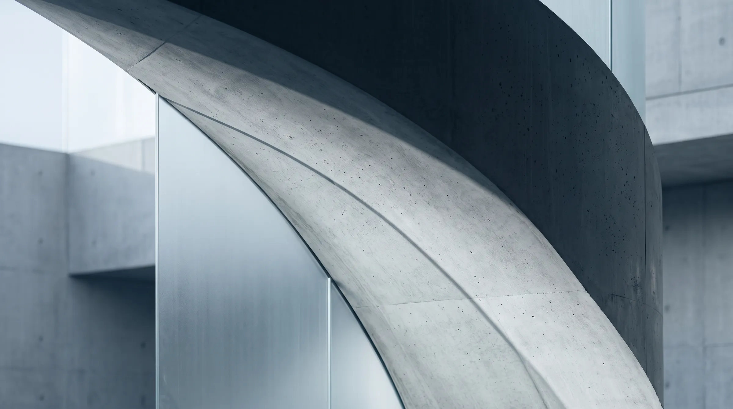 Two nested curves of board-formed concrete meeting brushed metal under cool daylight